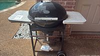 Front view of kettle grill showing lid, side shelves, wheels and frame