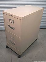 Front/side view of beige two-drawer metal filing cabinet on casters