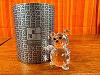 Front view of Swarovski crystal bear beside original tube
