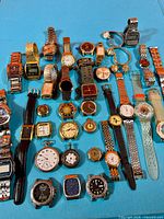 All watches laid out on blue surface – top view of entire lot
