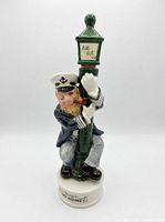 Full view of sailor figurine hugging green lamp post on white base