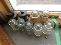 Nine electric insulators in a row including clear glass and brown ceramic types. Some glass insulators have chips and surface wear.