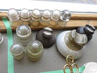 12 electric insulators of glass and ceramic materials with varied sizes and shapes placed on a surface.