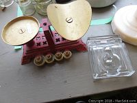 Glass ink well and cast metal scale model with brass weights shown side by side on surface.
