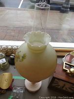 Full view of the oil lamp showing the painted floral cream glass globe with clear glass chimney on top.