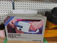 Photo showing Singer Stitch-Me-Quick hem and seam tacker box with product image and branding.