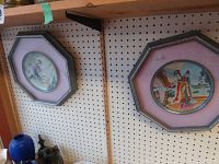 Two framed Asian style collector plates hung on pegboard. Both have octagonal dark wood frames and pink matte.