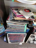 Photo showing a large pile of vinyl LP records and 45s on shelves, some with visible damage to sleeves. A variety of record sleeves can be seen stacked haphazardly.