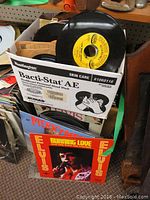 Box containing multiple vinyl records including LPs and 45s, visible album cover of Elvis Presley 'Burning Love'
