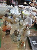 Complete set of oil lamps and chimneys on table with other kitchen/dining items in background.