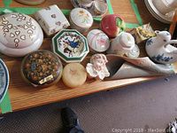 Photo showing 13 assorted trinket boxes and decorative ceramic items on a wooden tray with various shapes including round, octagonal, and rectangular.
