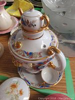 Photo of the white porcelain teapot with a lid showing red, blue, gold floral and leaf decoration and gold trimmed handles and knob.