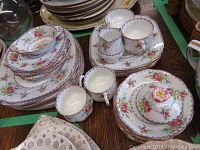 Full view of stacked china pieces including plates, teacups, creamer, sugar bowl, and small dish showing floral petit point design and gold trim.