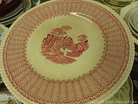Red transferware bowl marked Royal Tudor with detailed rural building scene and intricate patterned border. Shows age wear.