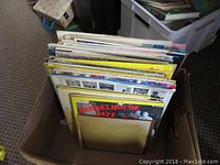 Box of assorted vintage vinyl LP records, stored upright showing edges and spines of multiple albums.