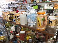 Wide view of various vintage beer steins, pottery, glass items on a shelf at a resale shop.