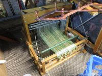 Overview of the wooden and metal weaving loom with thread in an industrial or storage setting.