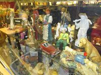 Top shelf display of various figures including Asian, elderly male, and female figurines, Disney character figures, and a small red toy car.