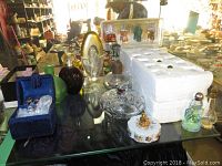 Multiple perfume bottles of differing sizes and styles on glass shelf, some with colored liquids, two matching boxes of empty miniature bottles, round Limoges box, green and purple bottles.