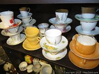 18 teacups and saucers including solid color and floral designs arranged on shelf
