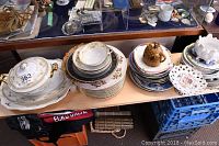 Wide view showing stacks of dishes, plates, bowls, Brazilian and Wedgwood collector plates, and creamer on tabletop