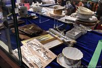 Blue cloth-covered tabletop display of assorted vintage and collectible items including ceramics, watches, a wallet, medals, epaulets, and stationery.