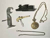 All five items laid out: pocket watch on chain, separate chain, cast iron train, parrot corkscrew, pistol keychain