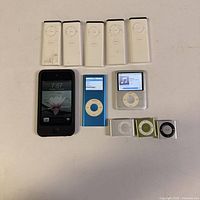 Overview of all five remotes, iPod Touch, blue Nano, silver click-wheel iPod, three Shuffles
