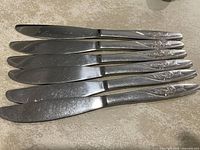 Six knives aligned showing handle rose motif and overall condition