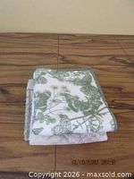 Folded white cotton towel with green floral pattern atop stack