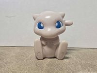 Front view of small pale pink Mew figure showing seated pose and blue eyes