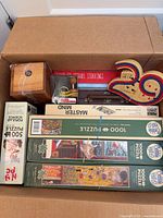 Box containing multiple Cobble Hill 1000-piece puzzles, Popular Science 500-piece puzzle, Mastermind game, backgammon board, wooden puzzle box