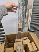 Full view of one clear glass cylindrical vase being held above shipping box