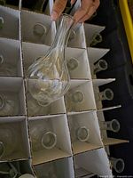 Box with cardboard dividers holding multiple identical clear glass bud vases, one lifted for view