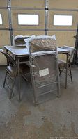 Folding table and four matching folding chairs, two chairs still in plastic wrap