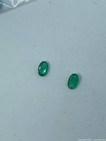 Two oval green gemstones on white surface