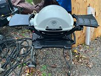 Front view of Weber portable grill on stand with side tables extended