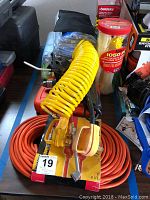 Photo showing orange heavy duty 100 ft extension cord and yellow coiled air compressor hose with air blow gun and container of nylon cable ties on top