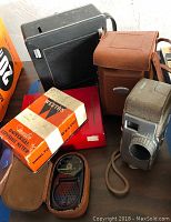 Three vintage light meters including a Weston Master Universal Exposure Meter in original box, one in brown leather case, and vintage cameras.