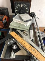 Showing collection of darkroom timer, books, rulers, numbering boards, and cutting tools arranged on table