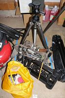 Tripod visible with metal legs and Gitzo tripod head, camera brackets next to it, yellow bag in front containing camera accessories