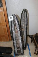 Photo showing two polished arrow-shaped stone sculptures with fossilized patterns standing side by side on the floor