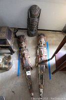 Photo showing the two detailed wood goddess carvings lying on the floor next to the painted blue tape for measurement reference and the carved mask behind them.