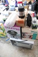 Stacked kitchen appliances including boxed Gourmia pressure cooker, Omega juicer, and Presorvac marinater with other small appliances visible.