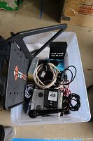 Plastic tote containing laptop stand, cables, boxed headset, audio interface, microphone and effects pedals