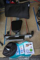Top view of multi-form rowing machine showing padded seat, footrests, resistance bands, yoga pillow and VacuPractor cushion on floor