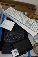 Apple keyboard, Brookstone Bluetooth keyboard, Kindle Fire tablet, and laptop case displayed together on a surface with some other items in background.