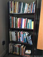 Books arranged on four shelves of wooden bookcase, various titles visible