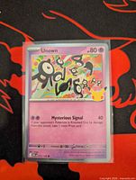 Front of Unown 072/128 holo card in sleeve and top-loader