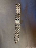 Full view of wristwatch laid flat showing entire bracelet and square dial
